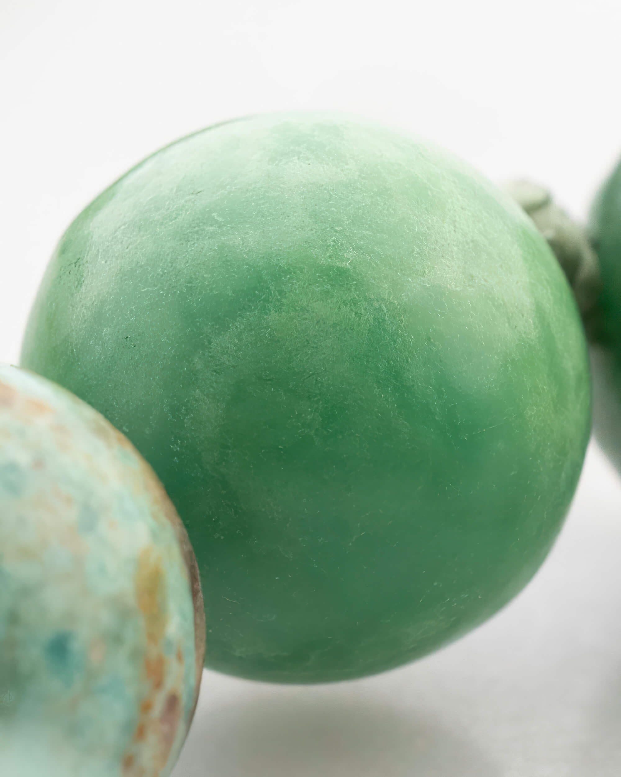 Detalle macro de una cuenta verde clara lisa junto a una cuenta jaspeada turquesa y naranja