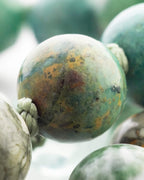 Detalle macro de una cuenta moteada en tonos oxido, verde y crema con vetas café