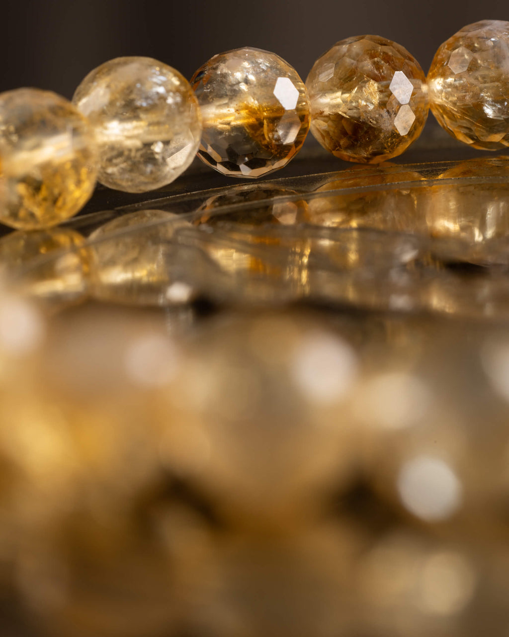 Cuentas facetadas de Citrino en fila con reflejo dorado sobre superficie espejada