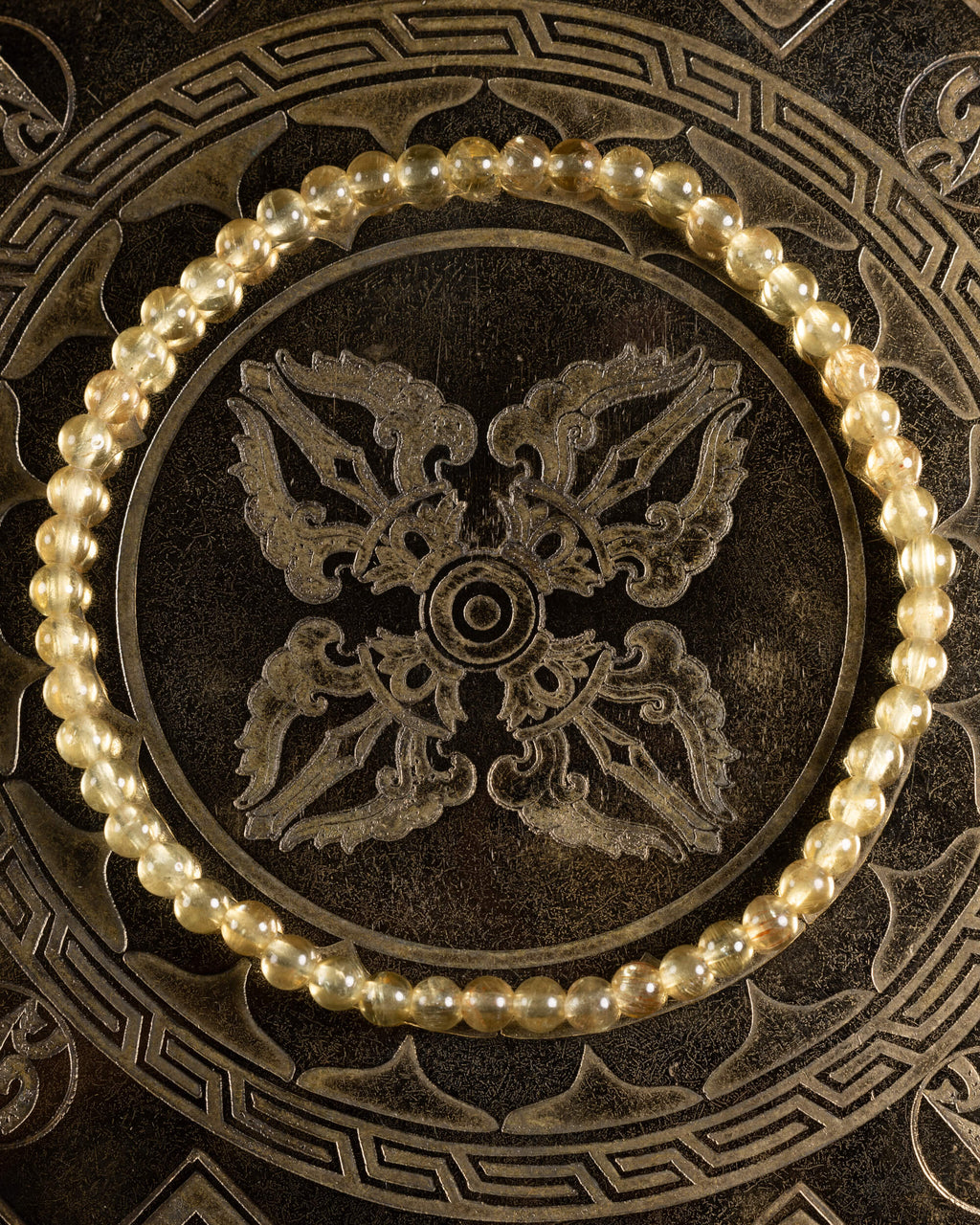 Pulsera de Cuarzo Rutilado de 4 mm, pieza completa sobre disco decorativo oscuro