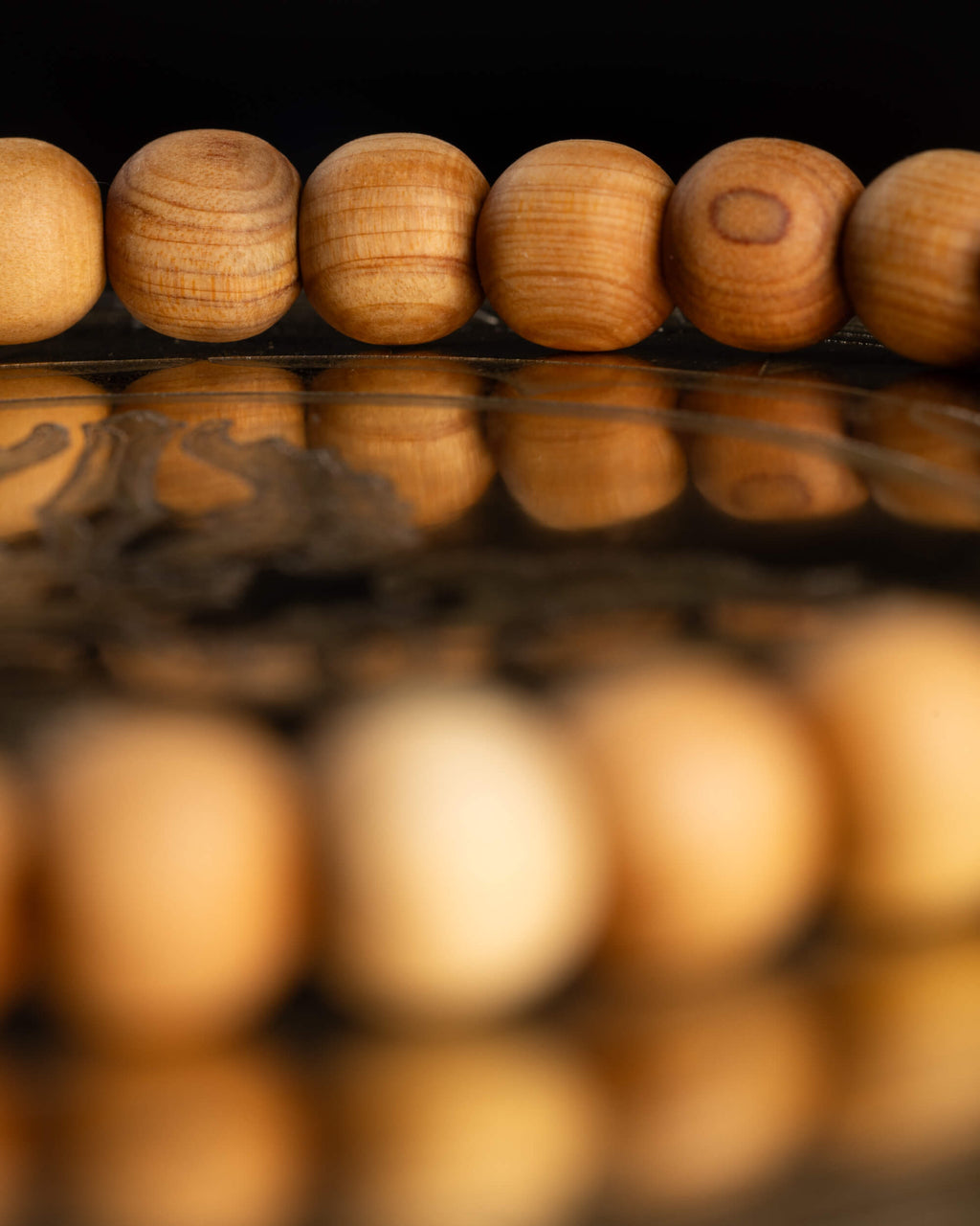 Cuentas de Madera de Sándalo en primer plano con reflejo sobre superficie oscura