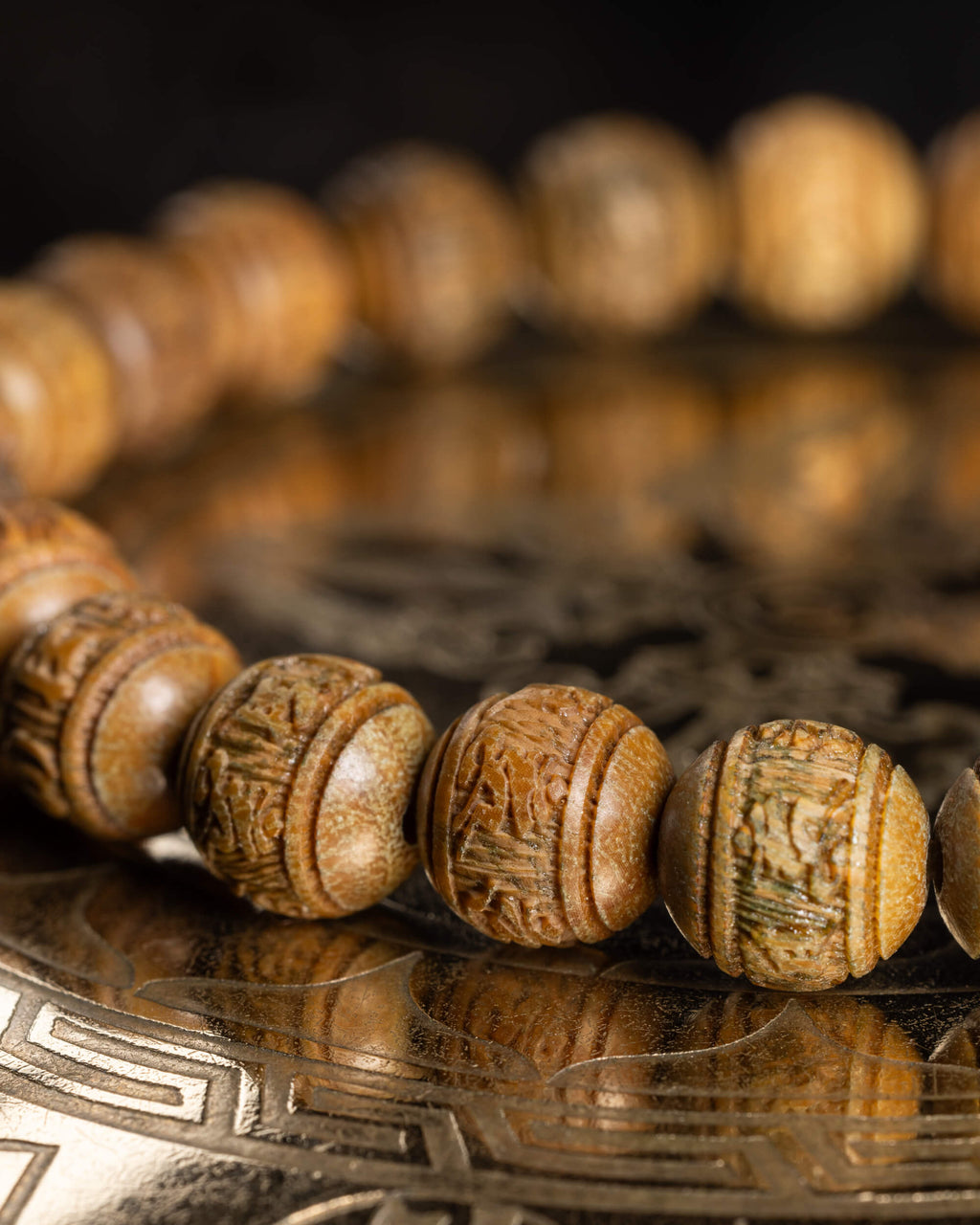Pulsera de Madera de Sándalo en curva, cuentas talladas con reflejo sobre superficie dorada