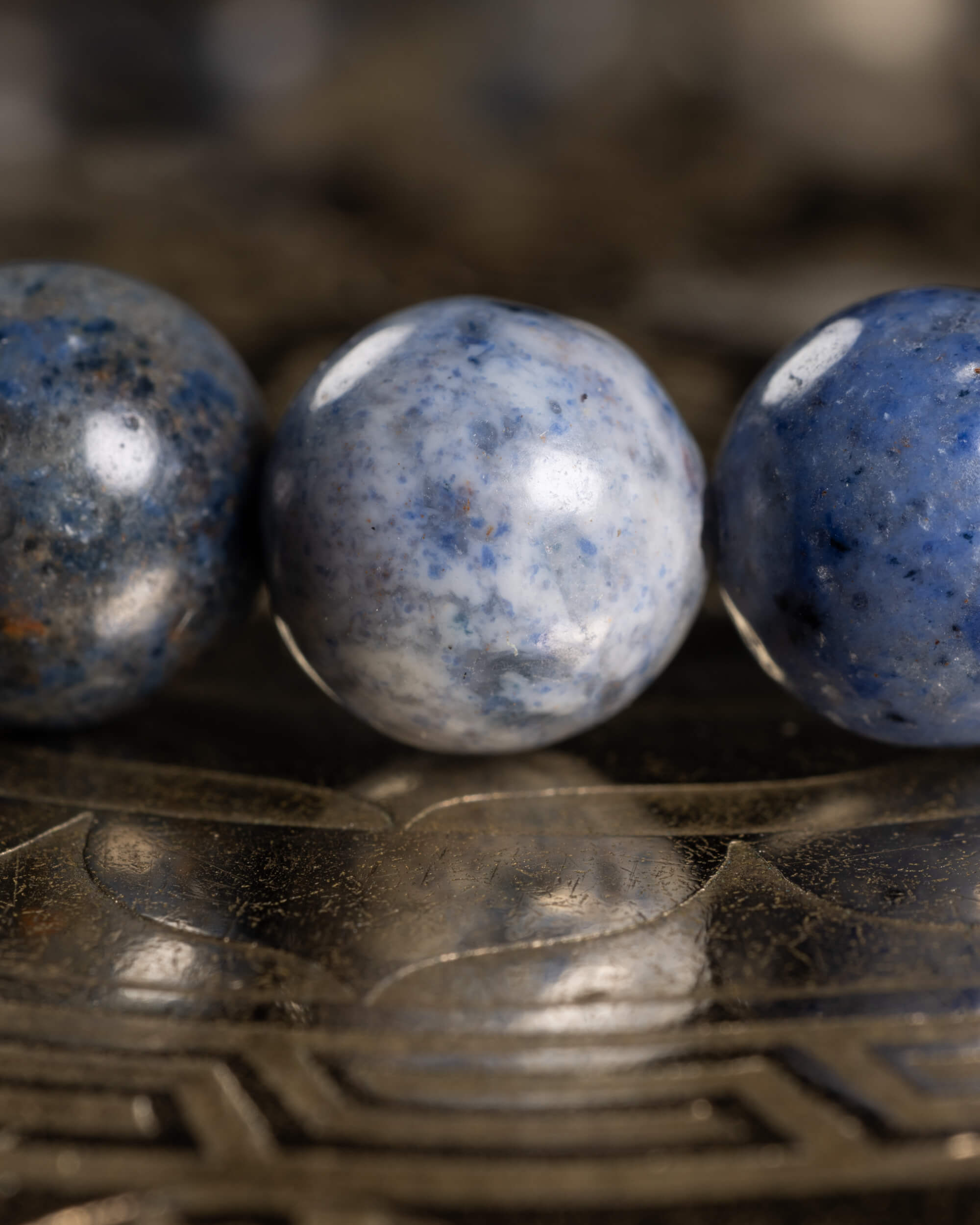 Detalle macro de tres cuentas de Dumortierita con moteado azul, gris y blanco