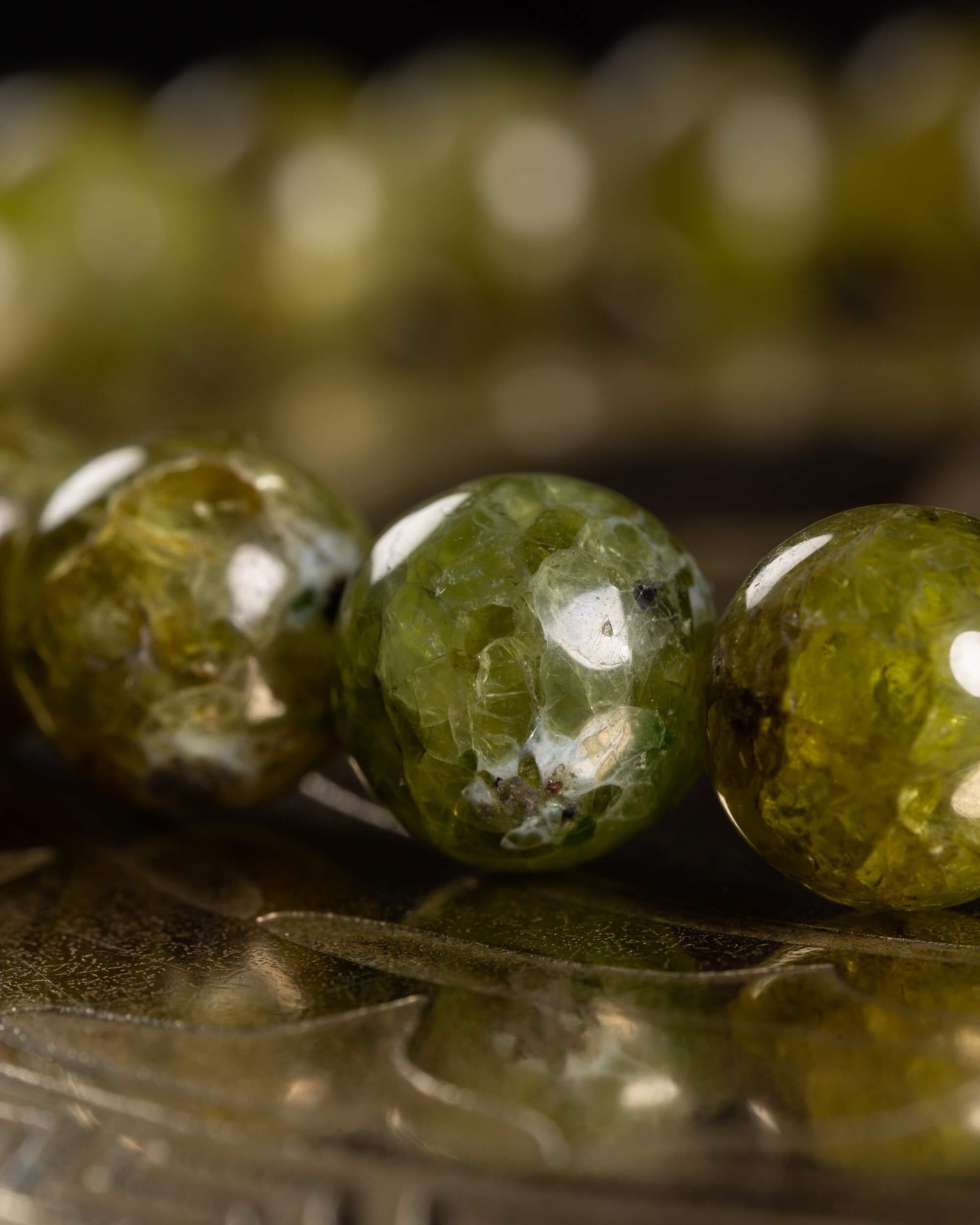 Pulsera de Peridoto en perspectiva, borde curvo de cuentas sobre superficie oscura