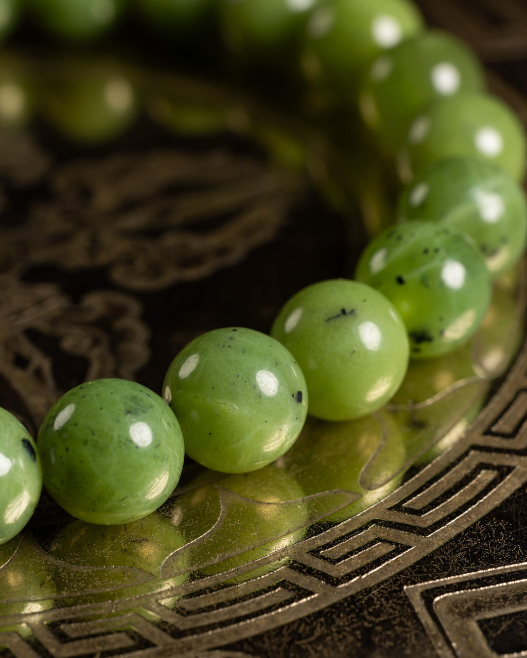 Detalle macro de las cuentas de Jade Verde sobre placa de bronce grabada