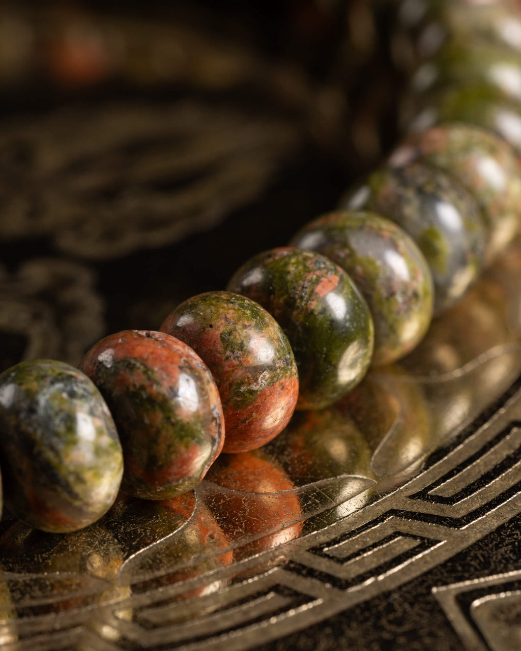 Pulsera de Jaspe Unakita en perspectiva, cuentas verde y rosa sobre soporte grabado