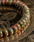 Pulsera de Jaspe Unakita en perspectiva cercana, curva de cuentas sobre soporte grabado