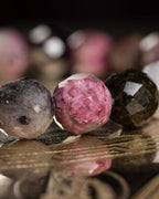 Detalle macro de tres cuentas facetadas de Turmalina en gris, rosa y verde oliva