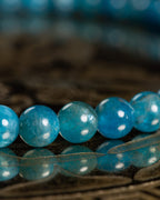 Detalle macro de las cuentas de Apatita Azul con brillo translúcido sobre madera