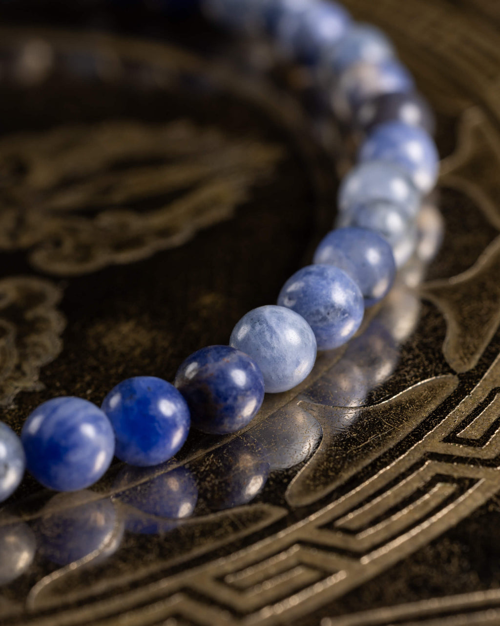 Pulsera de Sodalita en ángulo bajo, cuentas azules reflejadas en superficie oscura