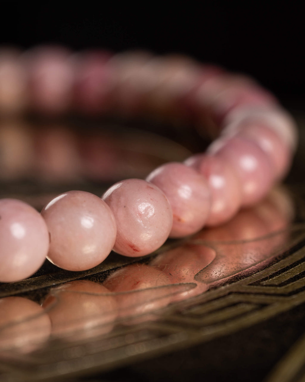 Pulsera de Rodonita Rosa en ángulo bajo, cuentas reflejadas en superficie metálica