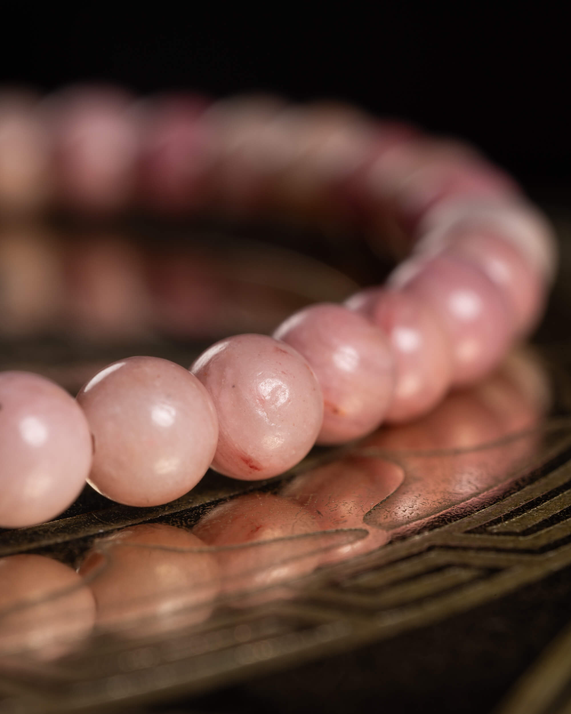 Pulsera de Rodonita Rosa en ángulo bajo, cuentas reflejadas en superficie metálica