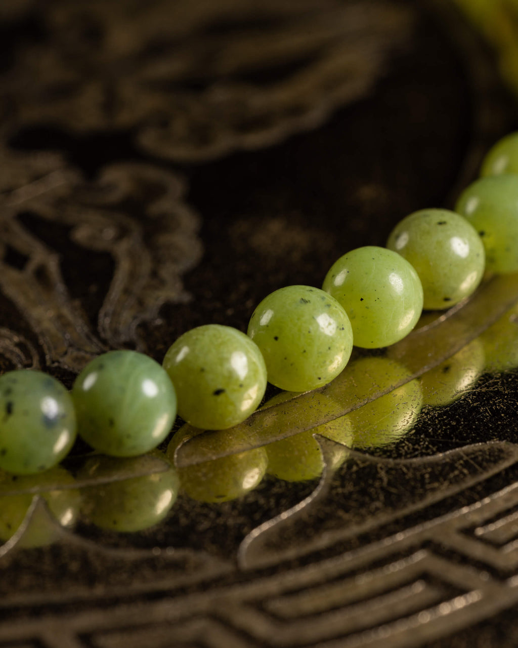 Detalle macro de las cuentas de Jade Verde con vetas oscuras sobre superficie metálica