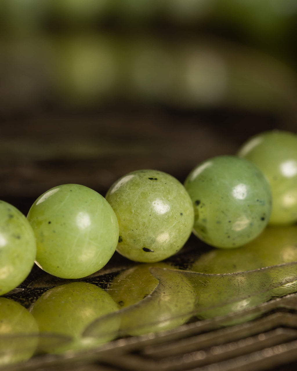 Detalle macro de las cuentas redondas de Jade Verde con su reflejo sobre la placa metálica