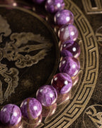 Pulsera de Lepidolita Violeta en ángulo, cuentas moradas alineadas sobre bandeja grabada