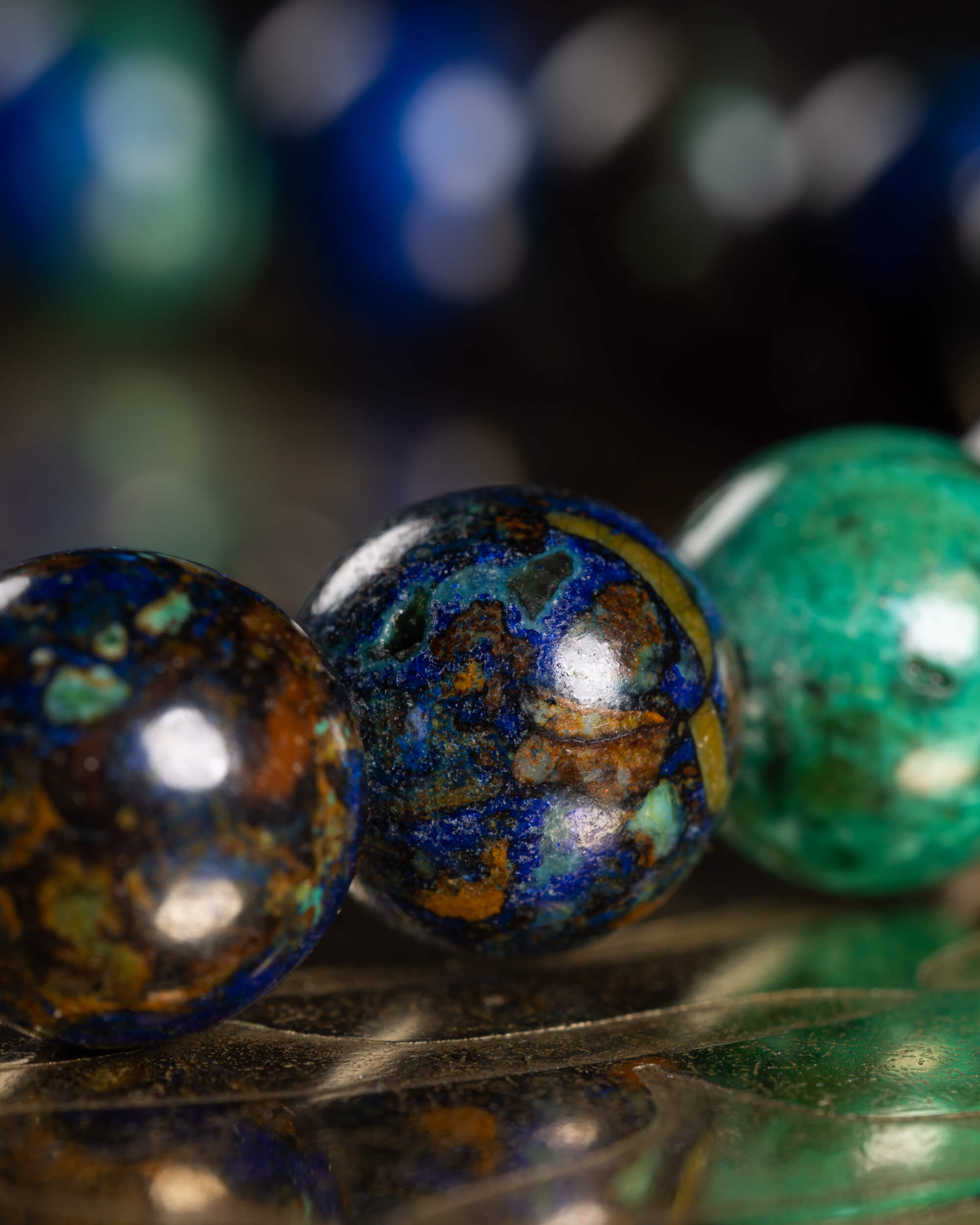 Detalle macro de tres cuentas de Crisocola con vetas cafés, azules y verdes