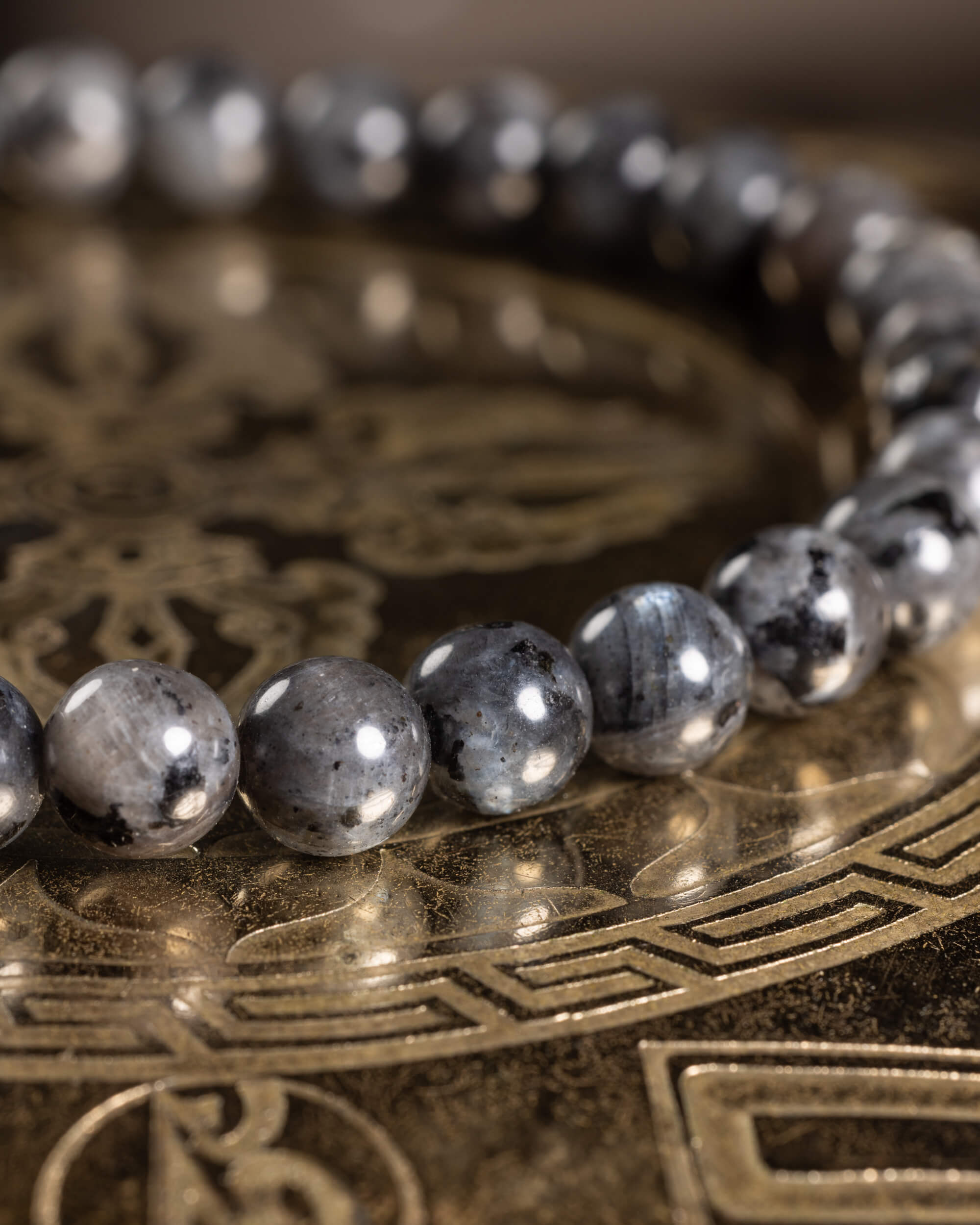 Pulsera de Larvikita en ángulo curvo sobre placa grabada, cuentas grises con brillo metálico