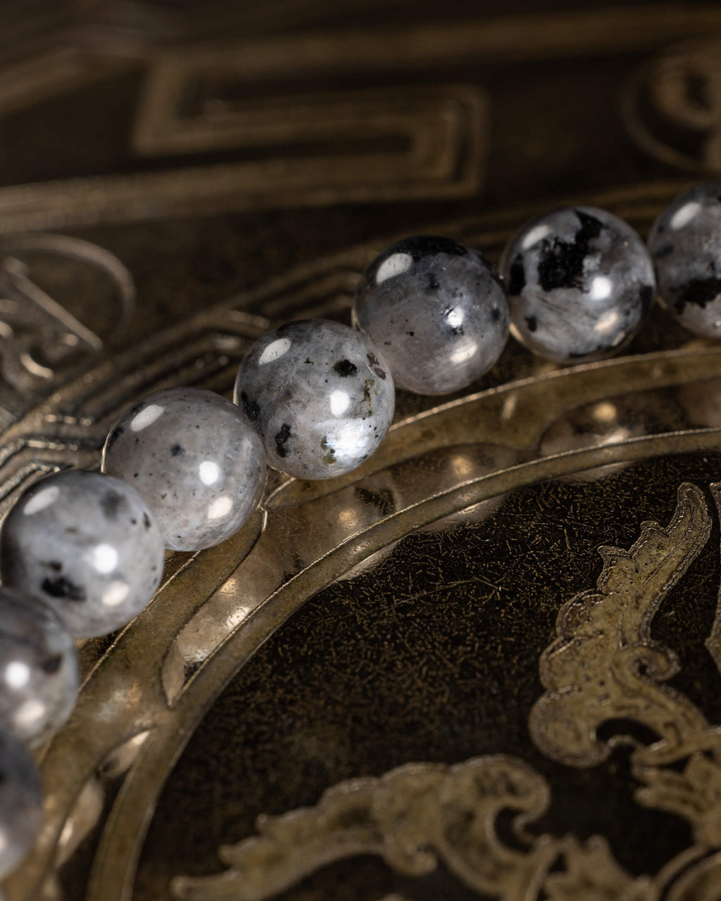 Pulsera de Larvikita en perspectiva sobre placa dorada grabada con motivos orientales