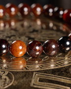 Pulsera de Granate Espesartina en fila sobre placa dorada, cuentas naranja y vino