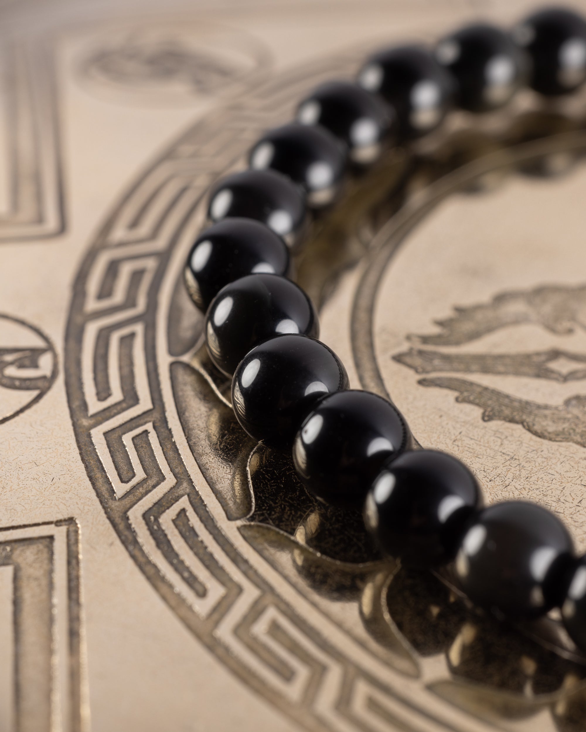 Pulsera de Obsidiana Arcoíris en ángulo, cuentas negras alineadas sobre bandeja grabada