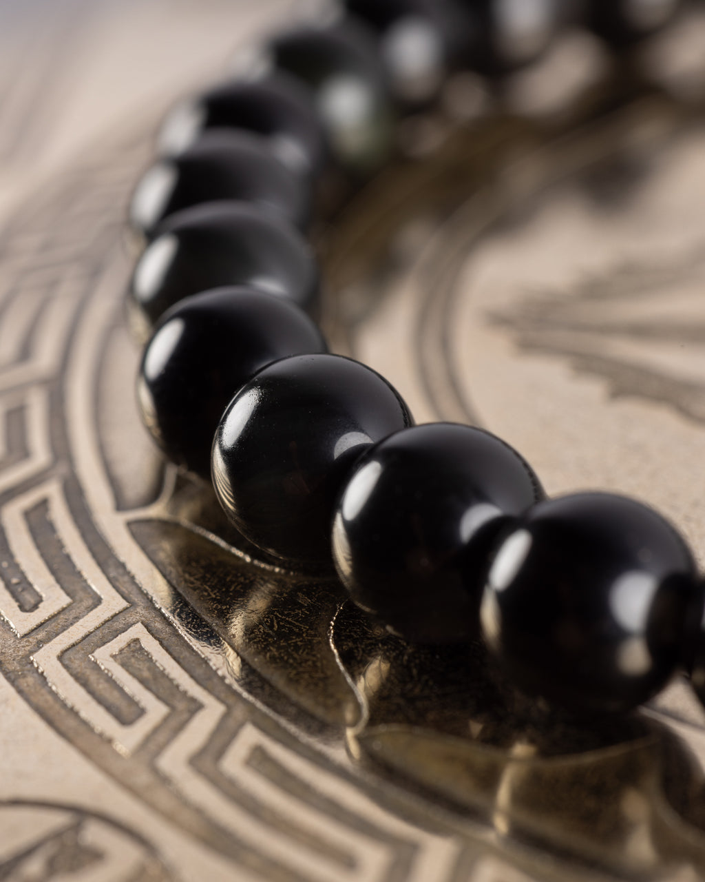 Pulsera de Obsidiana Arcoíris vista de perfil, curva de cuentas sobre bandeja grabada