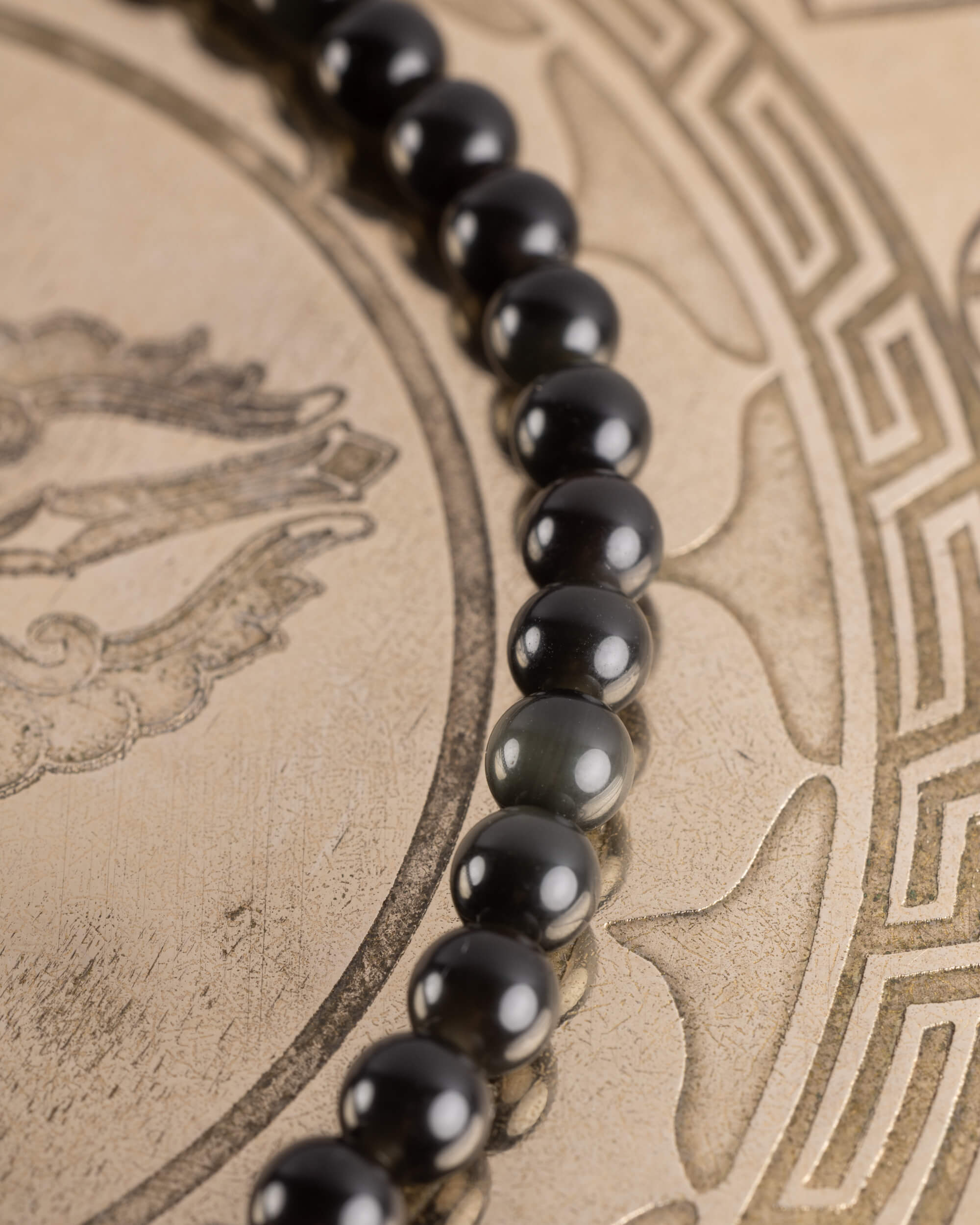 Pulsera de Obsidiana Negra en ángulo, cuentas alineadas sobre bandeja grabada