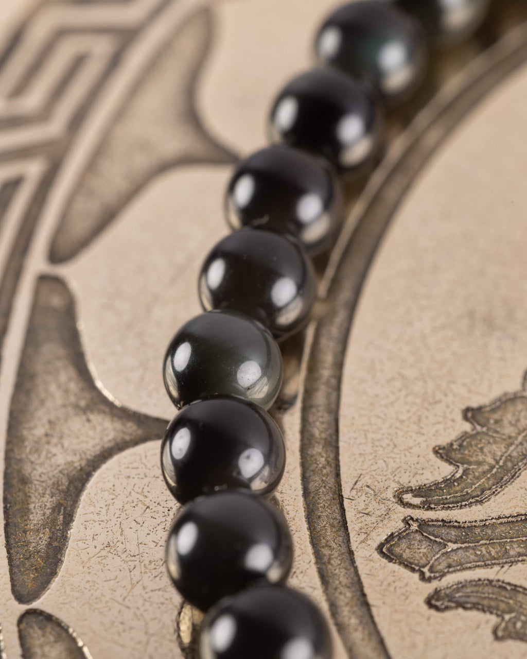Pulsera de Obsidiana Negra vista de perfil con reflejos dorados de la bandeja
