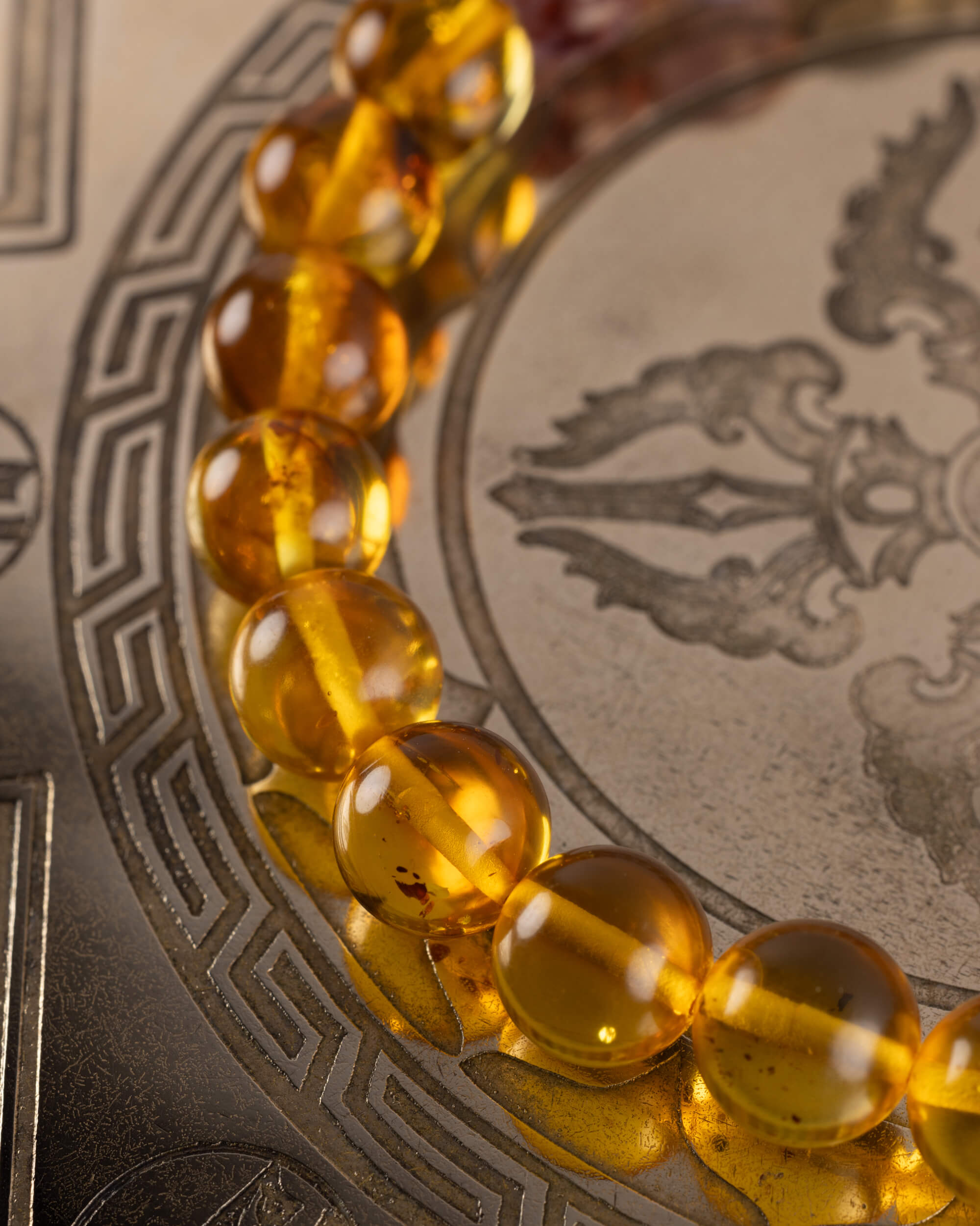 Detalle macro de las cuentas de Amatista Fantasma de la pulsera Mithra, con una esfera de Ámbar desenfocada al fondo