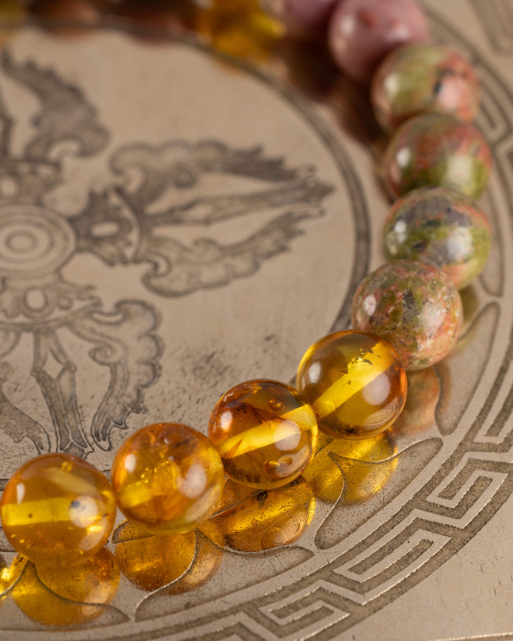 Detalle macro de las cuentas de Ámbar y Jaspe Unakita de la Pulsera Dazbog sobre placa grabada