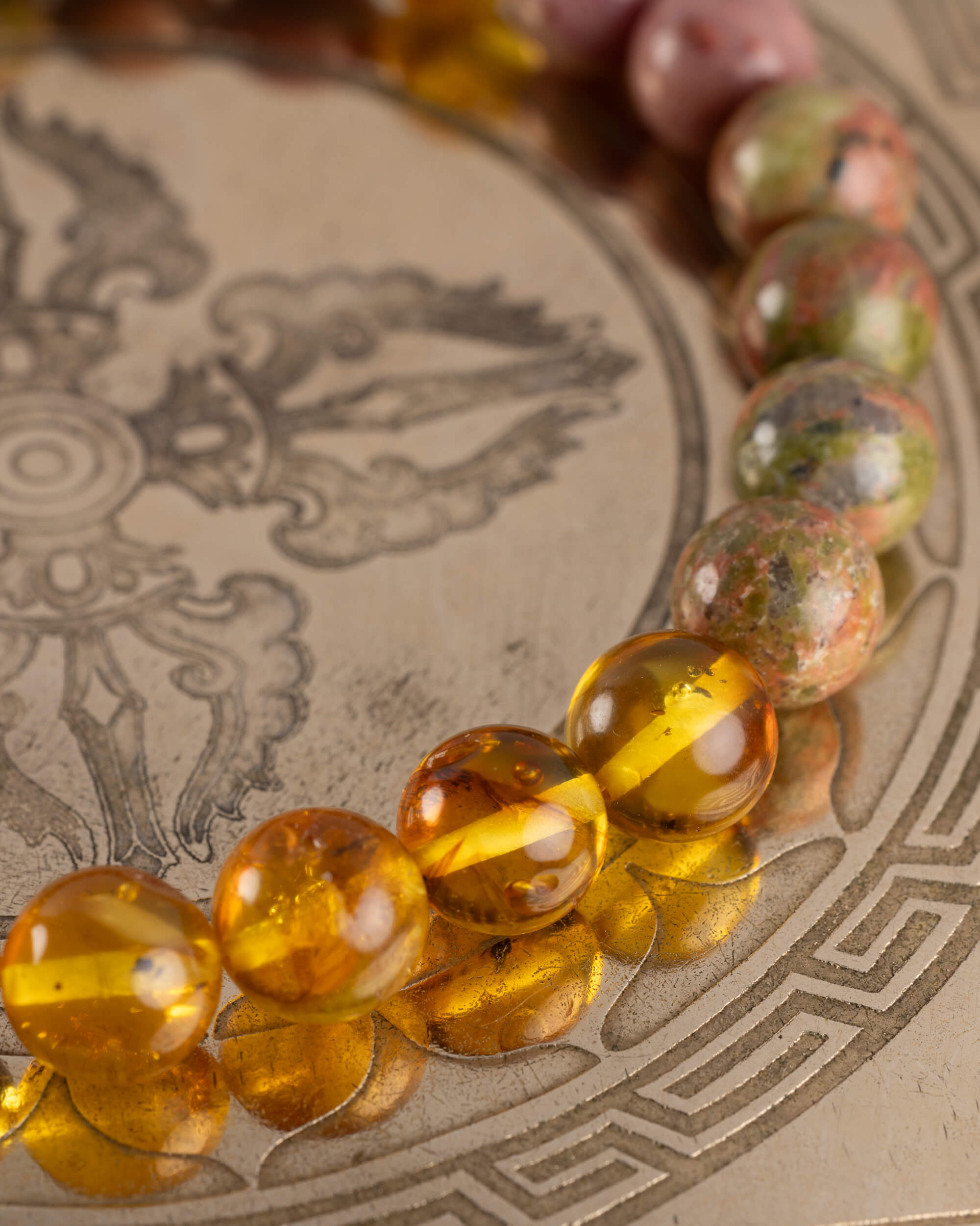 Detalle macro de las cuentas de Ámbar y Jaspe Unakita de la Pulsera Dazbog sobre placa grabada