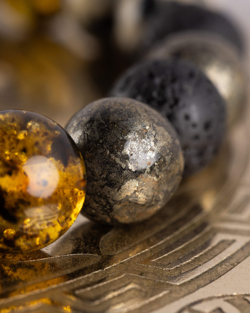 Detalle macro de las cuentas de Ámbar, Pirita y Piedra Volcánica de la Pulsera Malakbel sobre placa grabada