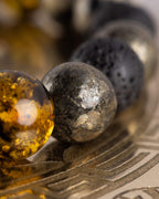 Detalle macro de las cuentas de Ámbar, Pirita y Piedra Volcánica de la Pulsera Malakbel sobre placa grabada