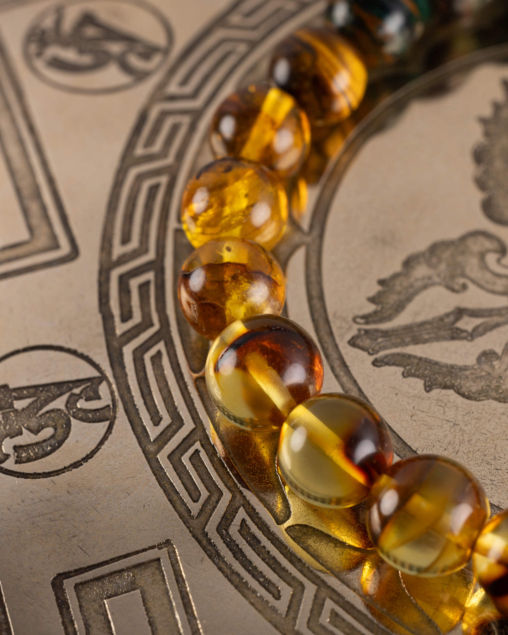 Detalle macro de las cuentas de Ámbar y Ojo de Tigre de la Pulsera Freyr sobre placa grabada