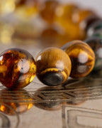 Detalle macro de las cuentas de Ámbar y Ojo de Tigre de la Pulsera Freyr sobre placa grabada