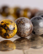 Detalle macro de una cuenta de ambar en primer plano junto a una esfera gris moteada, pulsera Yhi