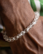 Pulsera de Cuarzo Transparente puesta en la muñeca junto a tela verde