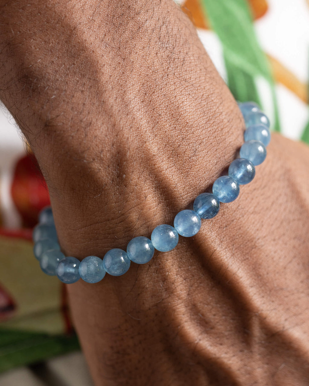 Pulsera de Aguamarina puesta en la muñeca, acercamiento con fondo de hojas verdes