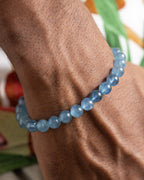 Pulsera de Aguamarina puesta en la muñeca, acercamiento con fondo de hojas verdes