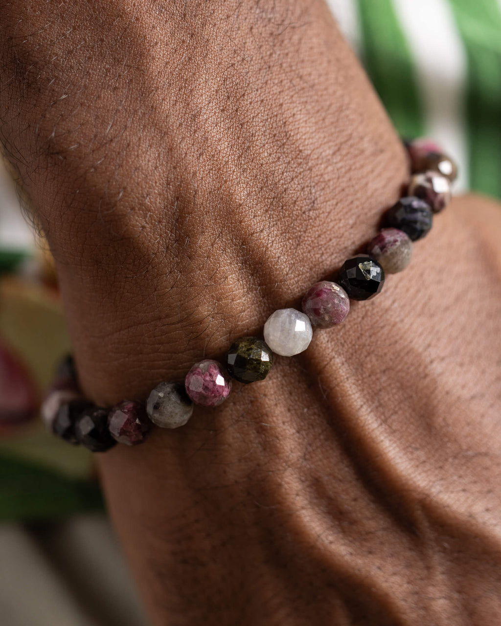 Pulsera de Turmalina Multicolor puesta en la muñeca, acercamiento con fondo verde