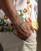 Pulsera de Apatita Azul puesta en la muñeca, con camisa estampada de hongos