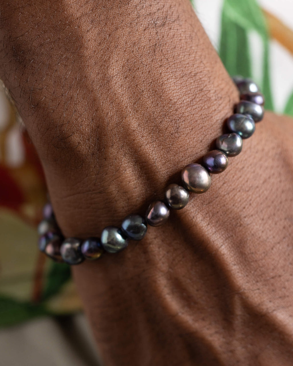 Pulsera de Perla Negra puesta en la muñeca sobre fondo con hojas