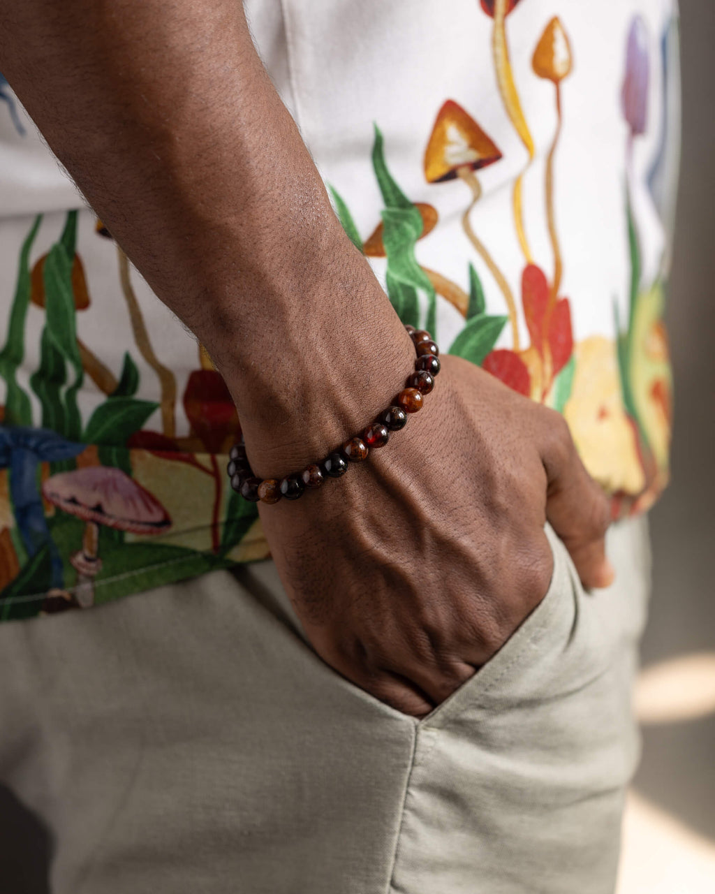 Pulsera de Granate Espesartina puesta en la muñeca, mano en el bolsillo con camisa estampada