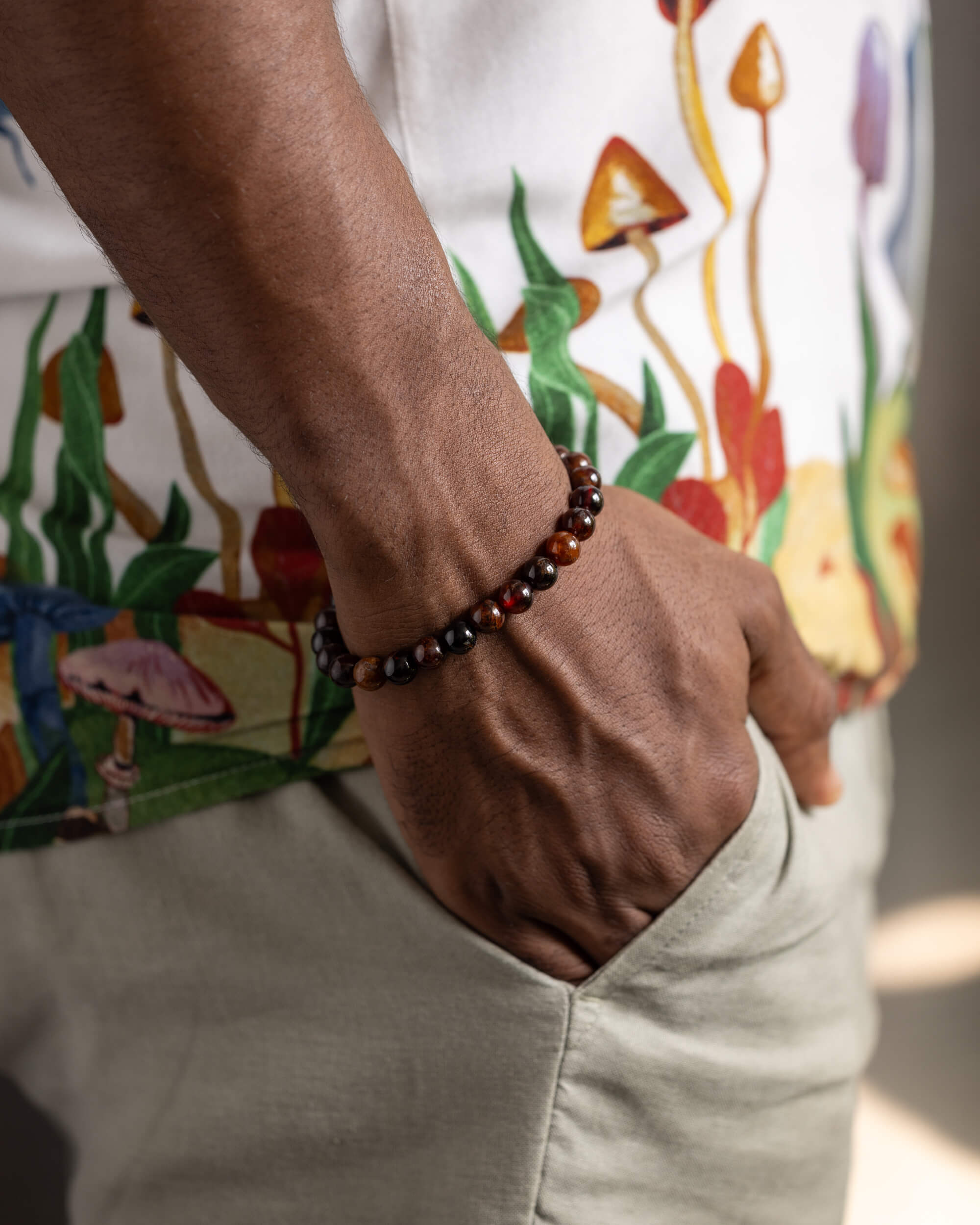 Pulsera de Granate Espesartina puesta en la muñeca, mano en el bolsillo con camisa estampada