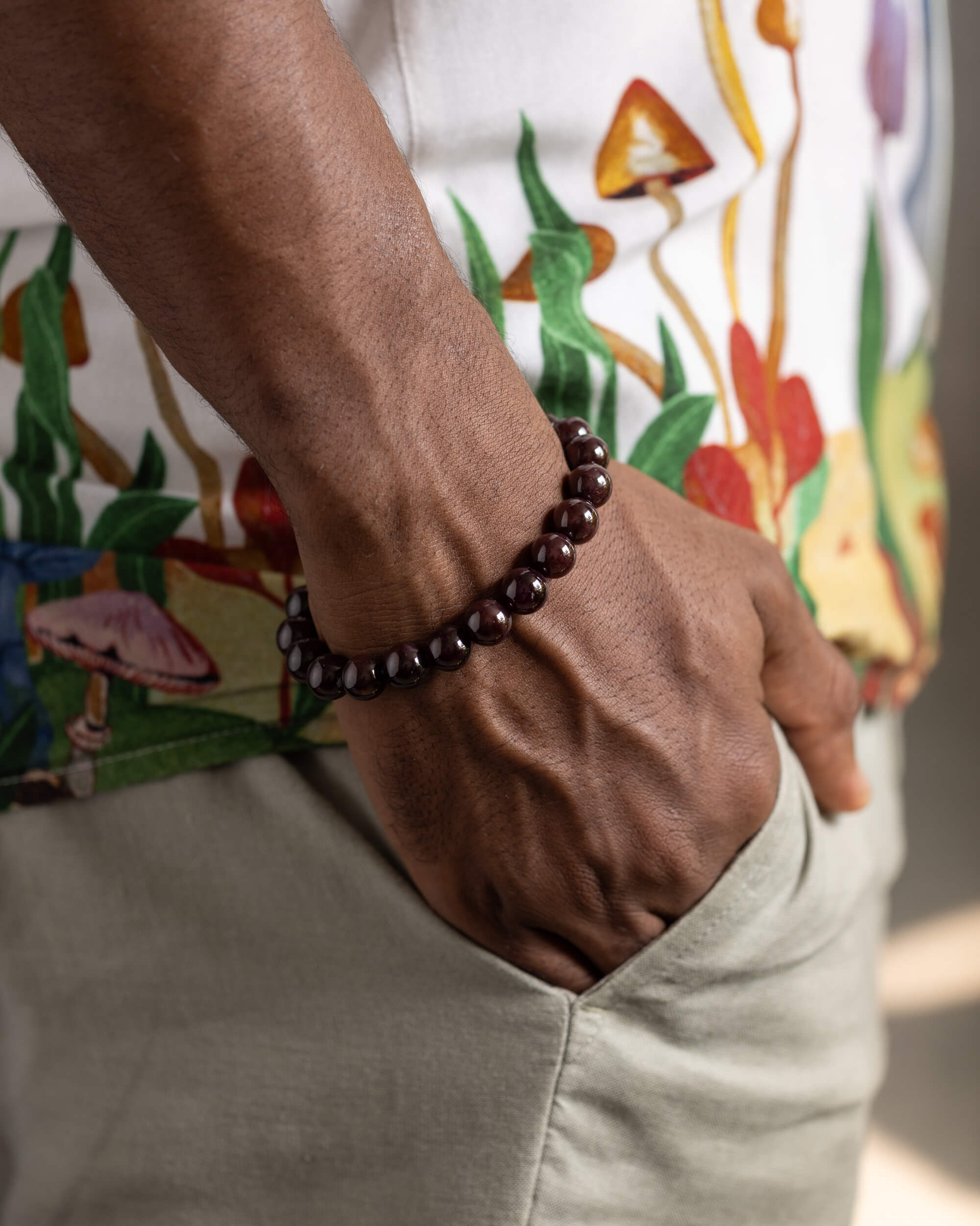 Pulsera de Granate Estrella puesta en la muñeca, mano en el bolsillo con camisa estampada