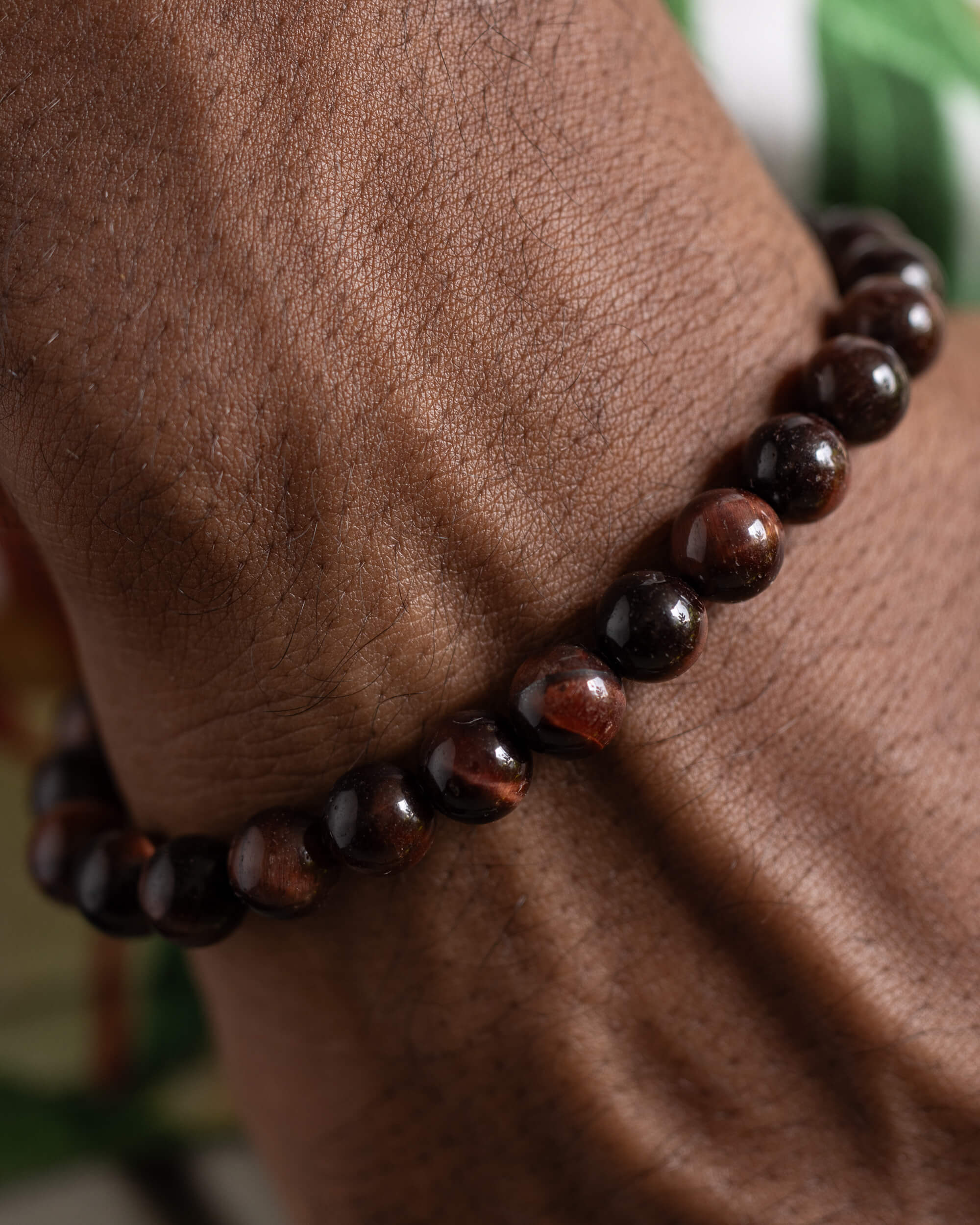 Pulsera de Ojo de Tigre Rojo puesta en la muñeca sobre fondo verde
