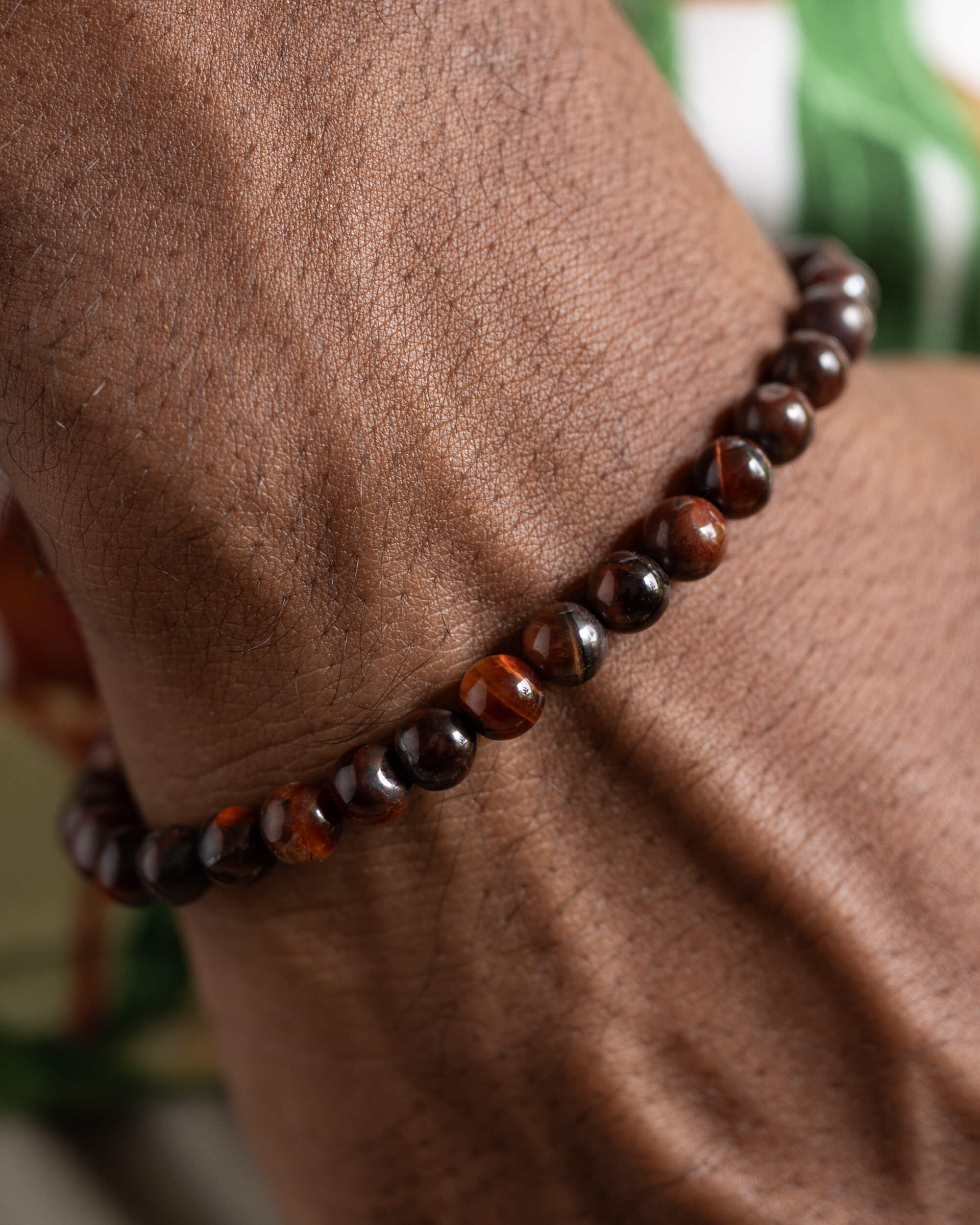 Pulsera de Ojo de Tigre Rojo puesta en la muñeca sobre fondo verde
