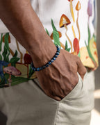 Pulsera de Cianita Azul puesta en la muñeca, con camisa de estampado de hongos al fondo