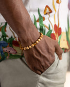 Pulsera de Madera de Sándalo puesta en la muñeca con un detalle de Ámbar, fondo floral
