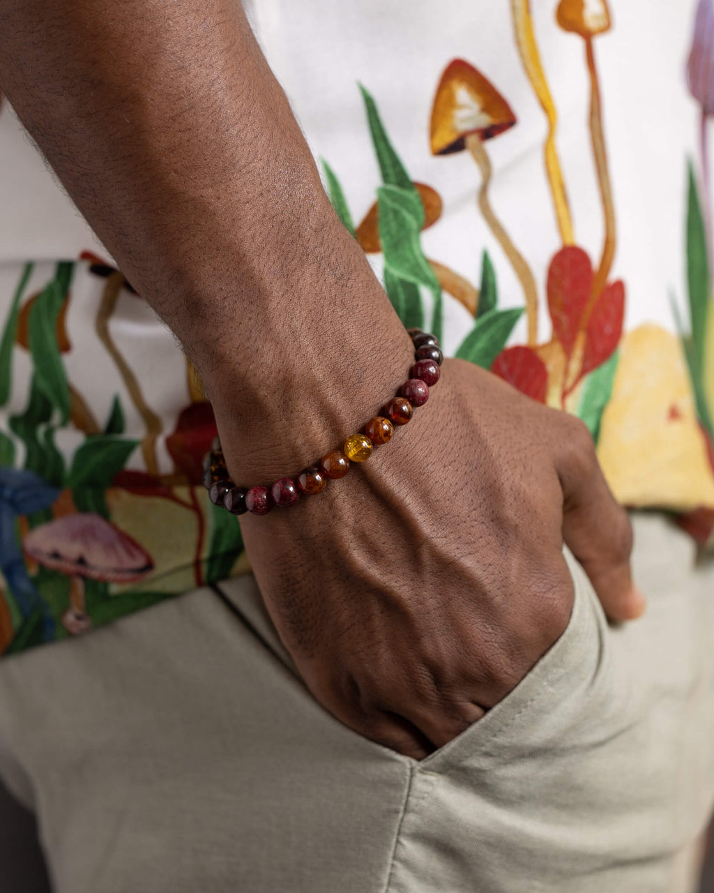 Pulsera Inti puesta en la muñeca, cuentas de granate y Ámbar sobre camisa estampada