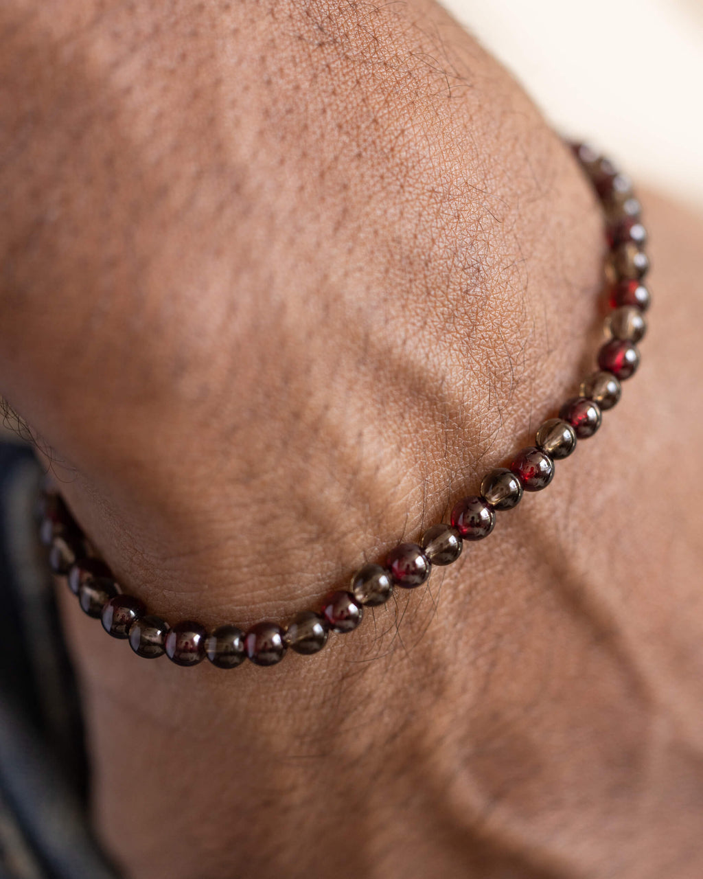 Pulsera de Granate Rojo y Cuarzo Ahumado puesta en la muñeca, mano en el bolsillo
